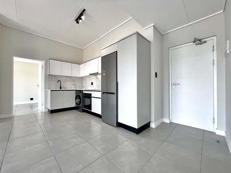 Modern kitchen featuring sleek white cabinetry, marble-look backsplash, integrated appliances, and neutral tiled flooring in an open-plan layout.