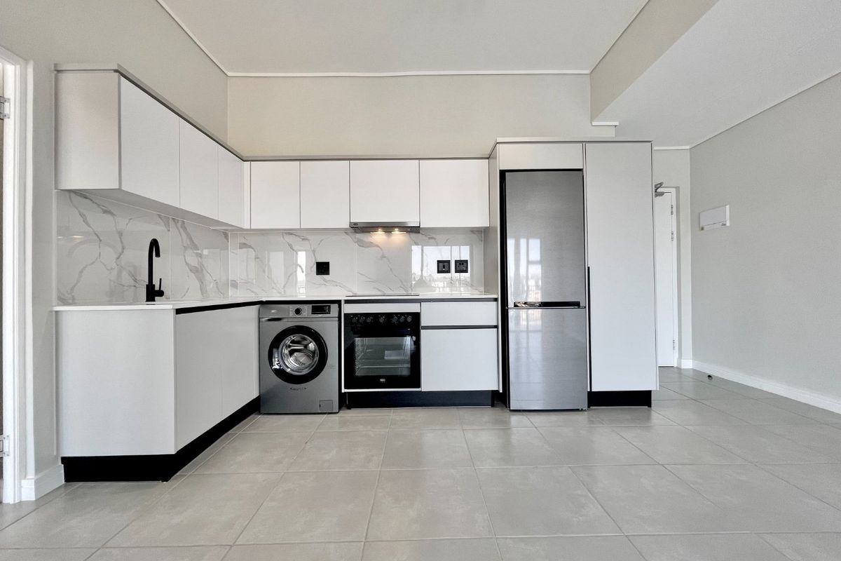 Modern, minimalist kitchen featuring sleek white cabinetry, marble-look splashback, integrated appliances, and neutral tiled flooring in an open-plan layout.