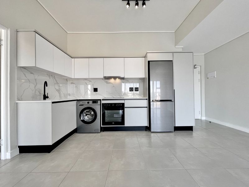 Modern, minimalist kitchen featuring sleek white cabinetry, marble-look splashback, integrated appliances, and neutral tiled flooring in an open-plan layout.