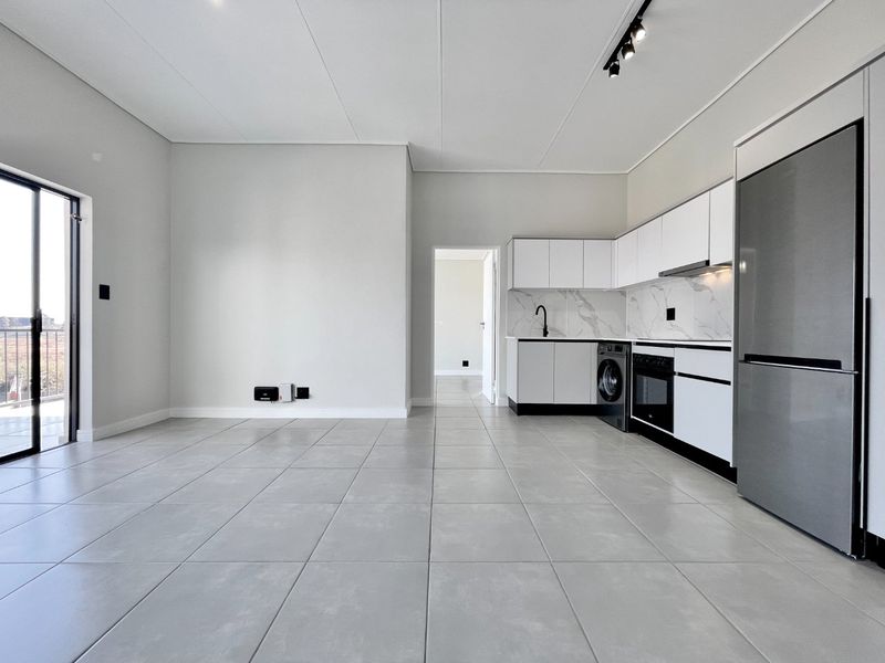 Modern open-plan living area featuring sleek tiled floors, a contemporary kitchen with marble-look backsplash, and direct access to a balcony through sliding glass doors.