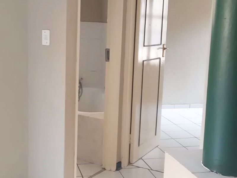 A neutral-toned hallway featuring white tiled flooring, leading to an adjacent bathroom and another room, presenting a clean and functional layout.