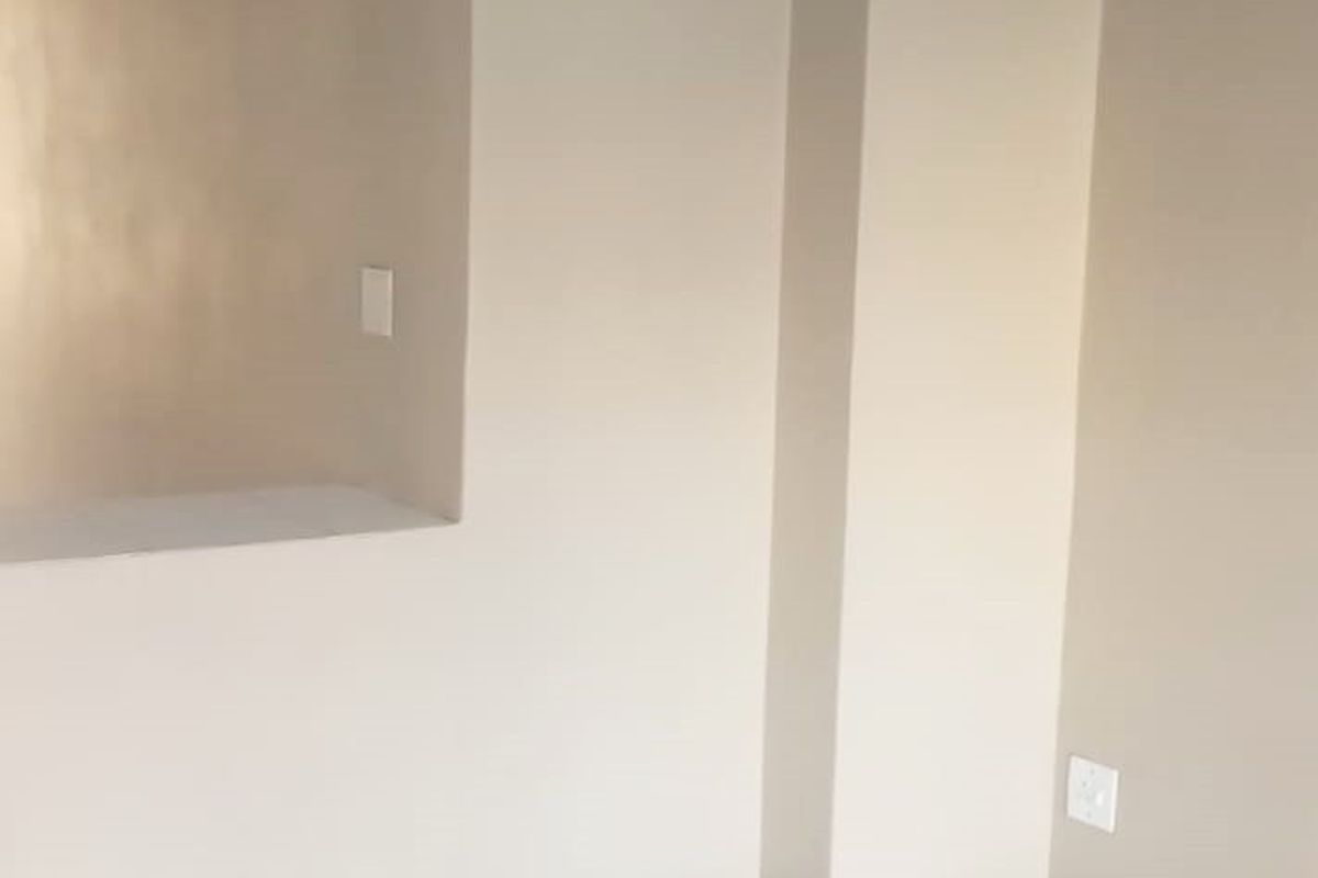 An empty living area featuring neutral wall paint, white tiled flooring, and green skirting boards, providing a clean and versatile space.