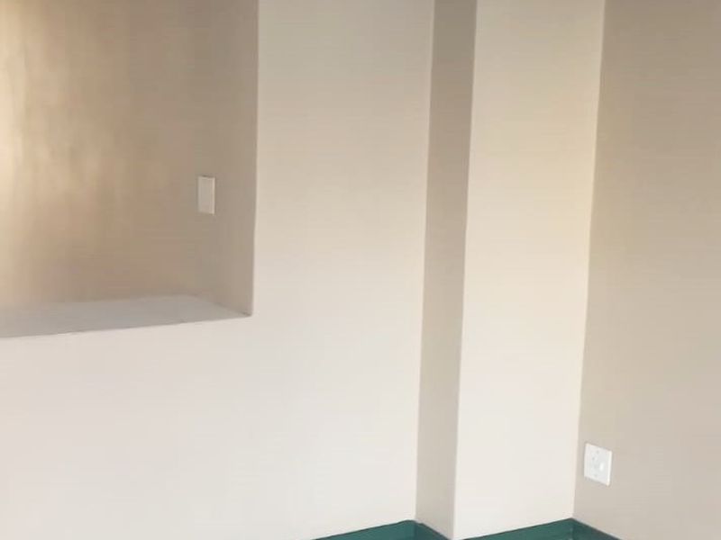 An empty living area featuring neutral wall paint, white tiled flooring, and green skirting boards, providing a clean and versatile space.