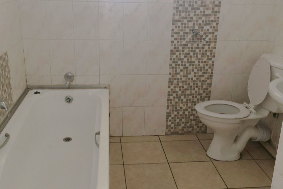 A functional bathroom featuring a built-in bathtub, toilet, and tiled finishes with a mosaic accent wall, requiring some maintenance and cosmetic updates.