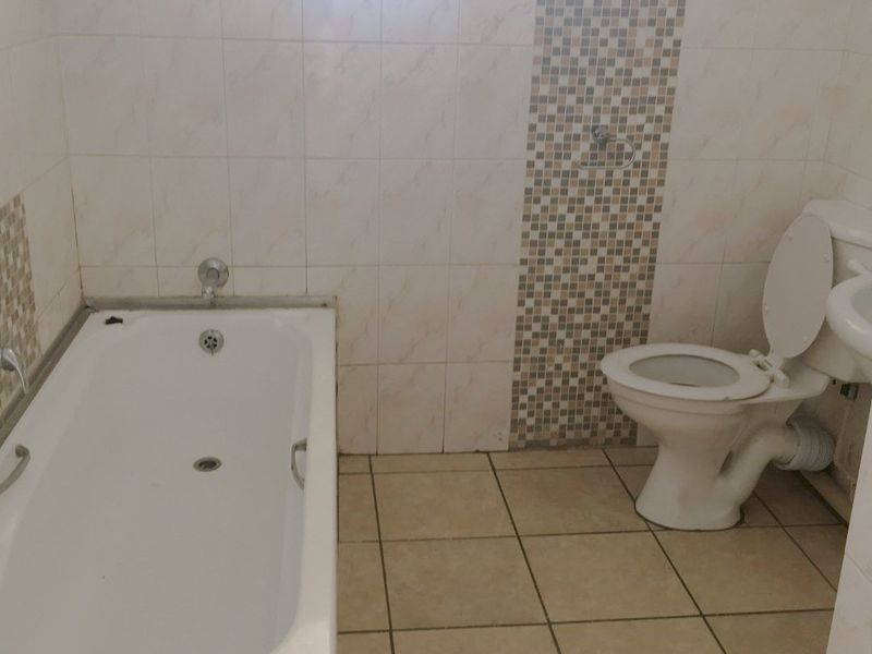 A functional bathroom featuring a built-in bathtub, toilet, and tiled finishes with a mosaic accent wall, requiring some maintenance and cosmetic updates.