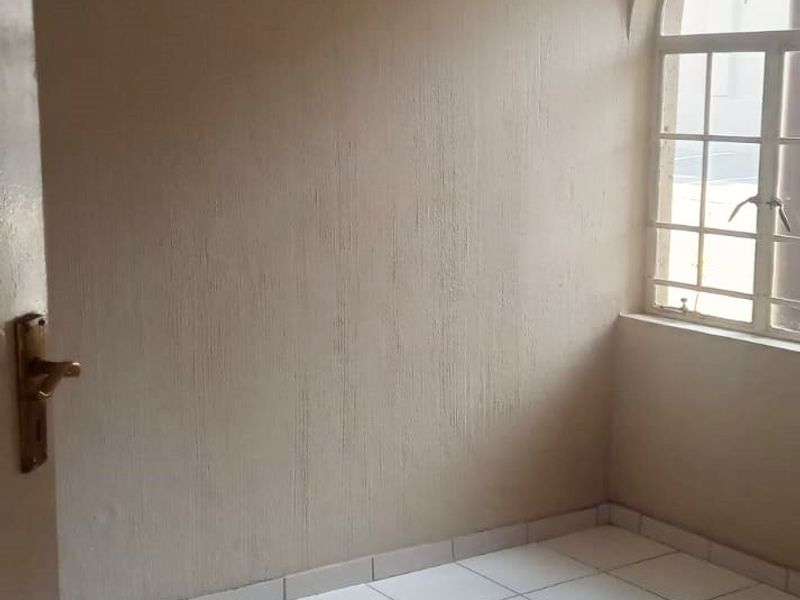 An empty bedroom featuring neutral textured walls, white tiled flooring, and a distinctive arched window providing natural light.