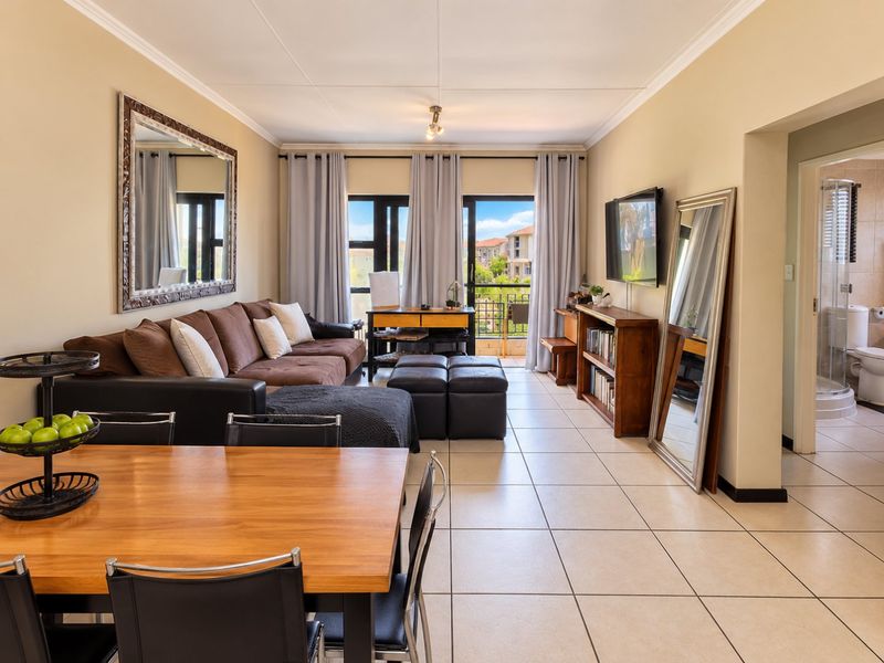 Spacious open-plan living and dining area featuring neutral tiled flooring, large sliding doors leading to a balcony, and access to an adjacent bathroom.