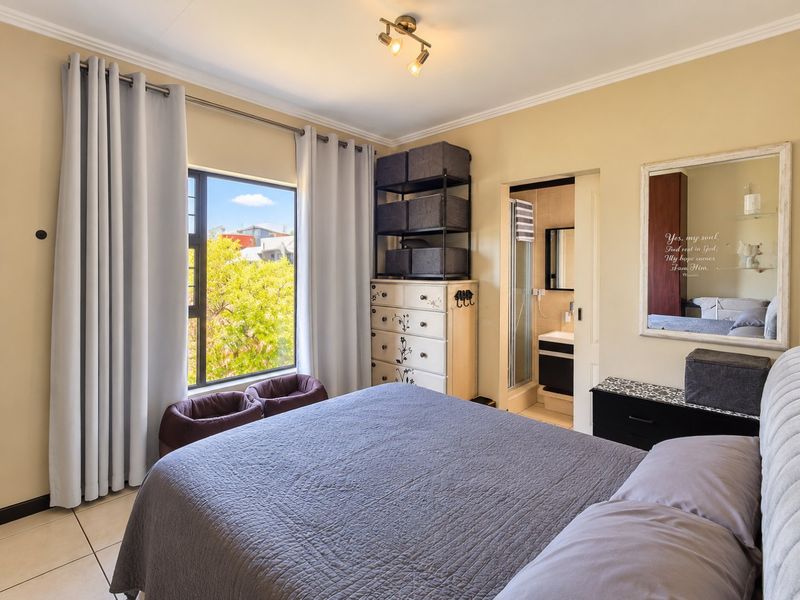 A well-maintained bedroom featuring tiled flooring, large window with natural light, and an adjoining en-suite bathroom.