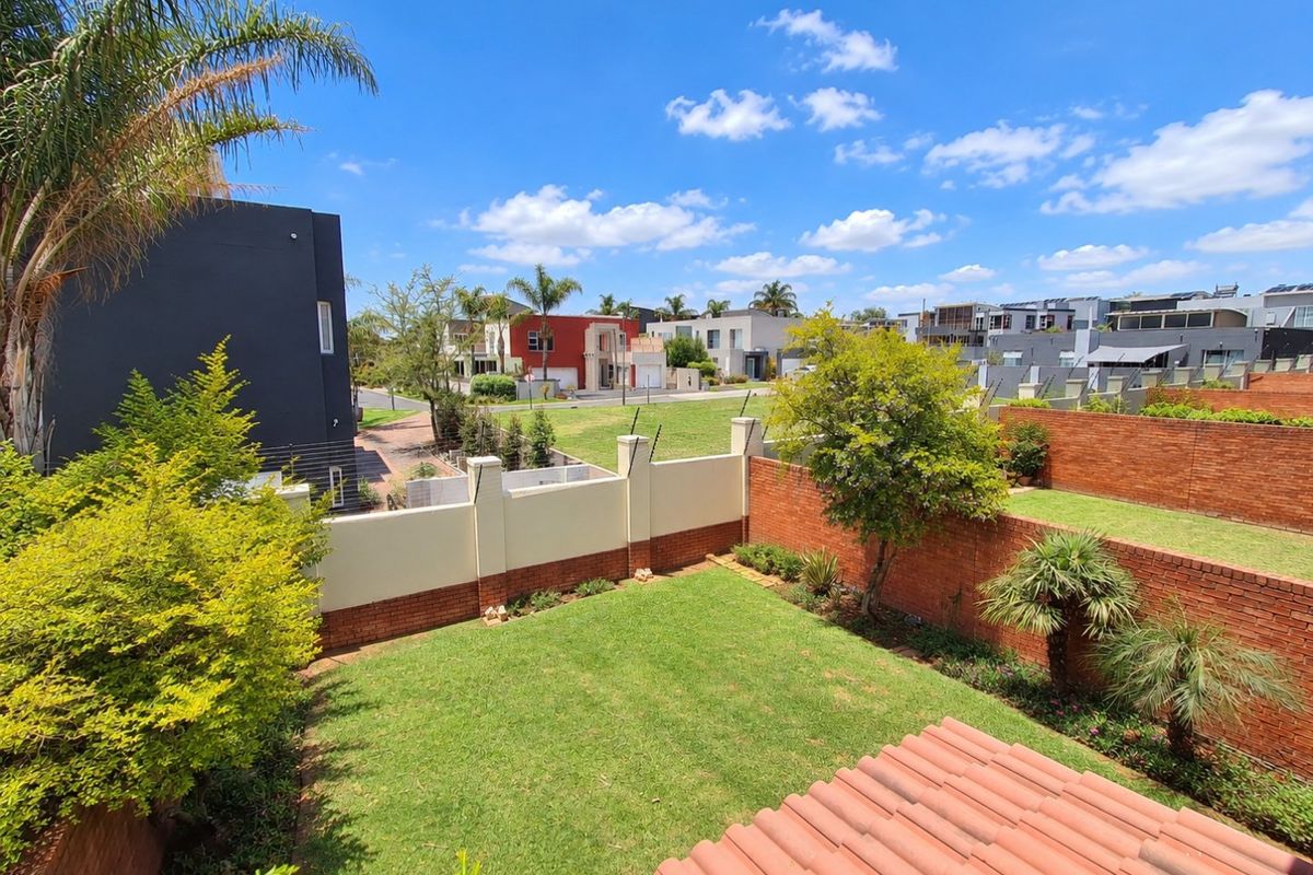 A view of a private rear garden featuring a well-maintained lawn, brick boundary walls with electric fencing, and a tiled roof section.