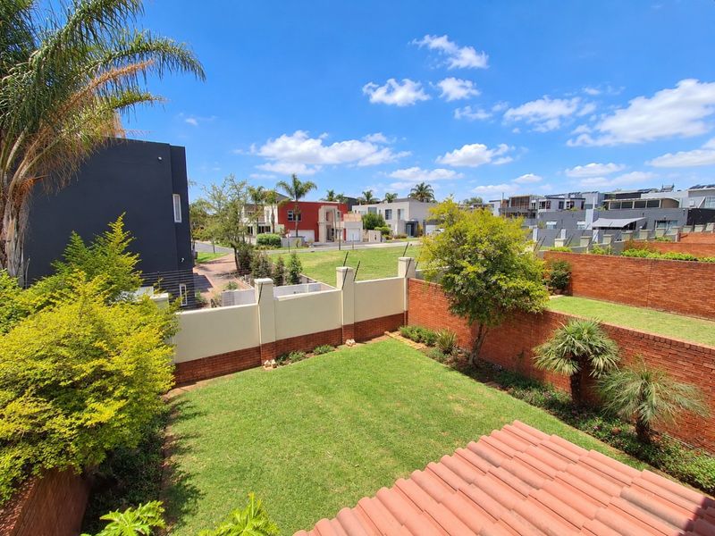 A view of a private rear garden featuring a well-maintained lawn, brick boundary walls with electric fencing, and a tiled roof section.