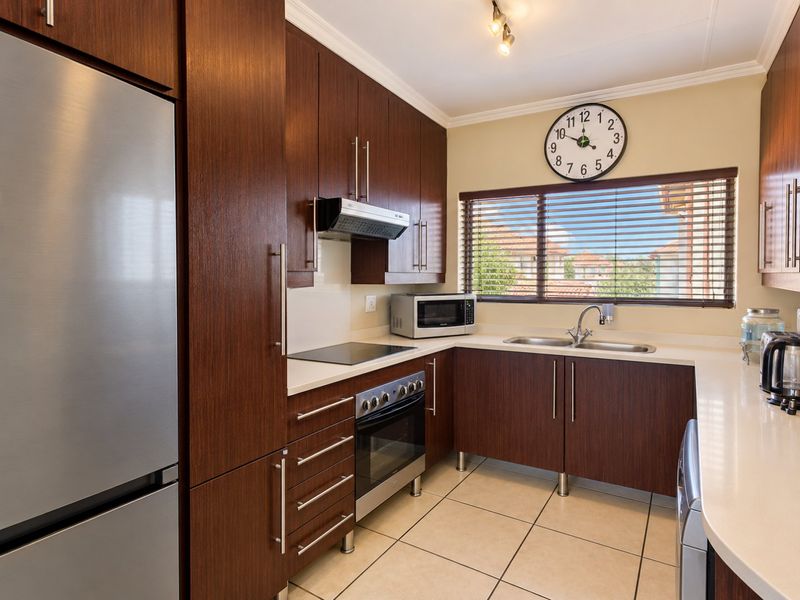 A well-maintained kitchen featuring dark wood cabinetry, stone countertops, integrated appliances, and tiled flooring with natural light from a window with venetian blinds.