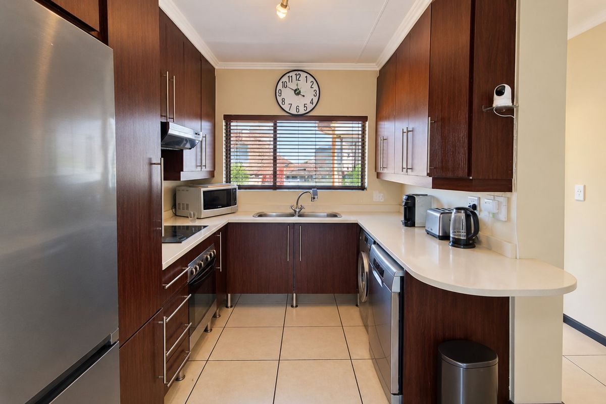 A well-maintained kitchen featuring dark wood cabinetry, stone countertops, tiled flooring, and integrated appliances, offering a functional and modern workspace.