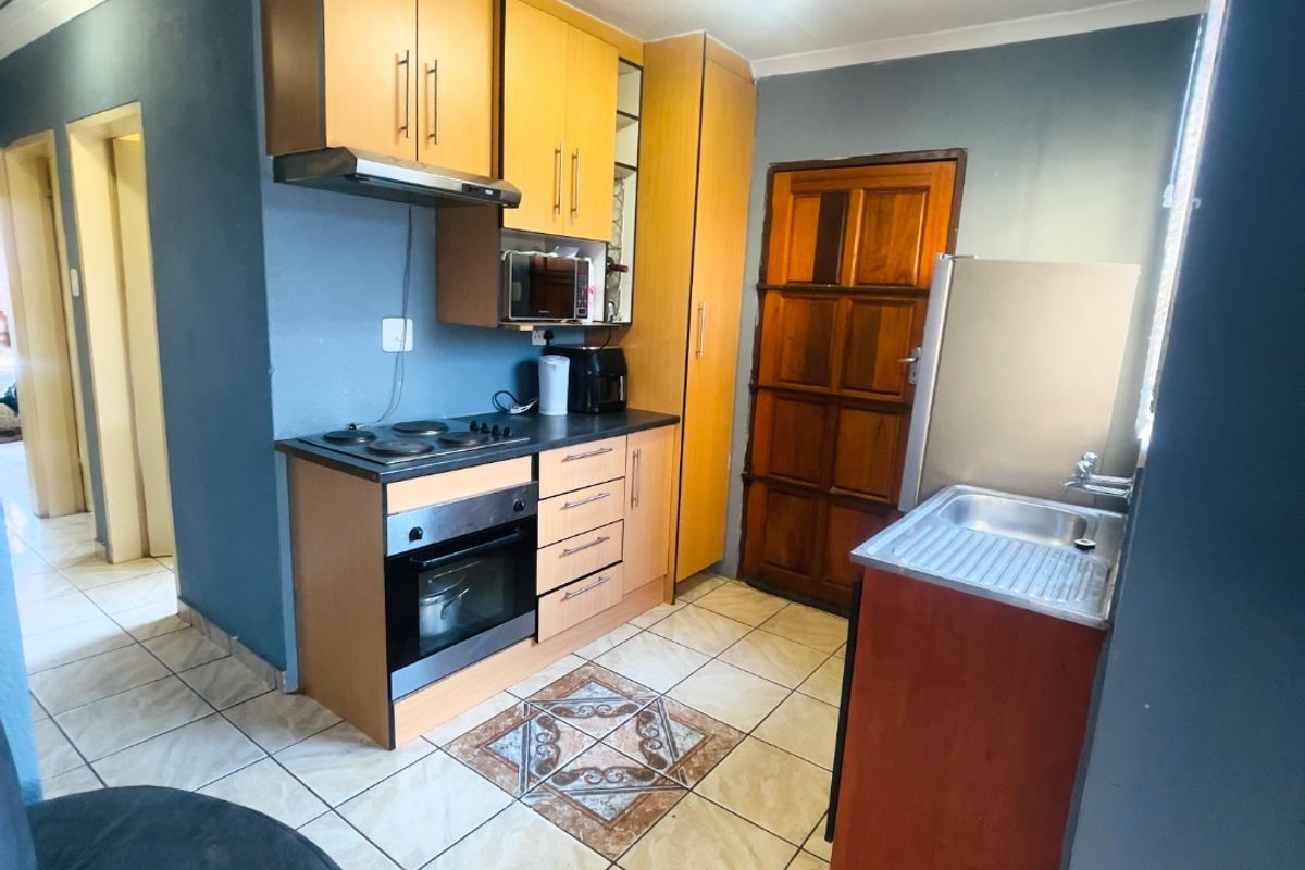 A functional kitchen featuring built-in wooden cabinetry, an integrated oven and hob, extractor fan, and a stainless steel sink with tiled flooring.