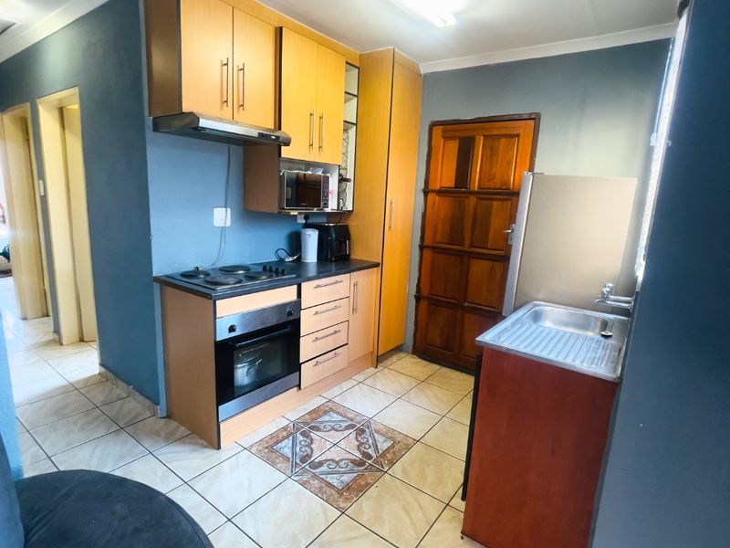 A functional kitchen featuring built-in wooden cabinetry, an integrated oven and hob, extractor fan, and a stainless steel sink with tiled flooring.