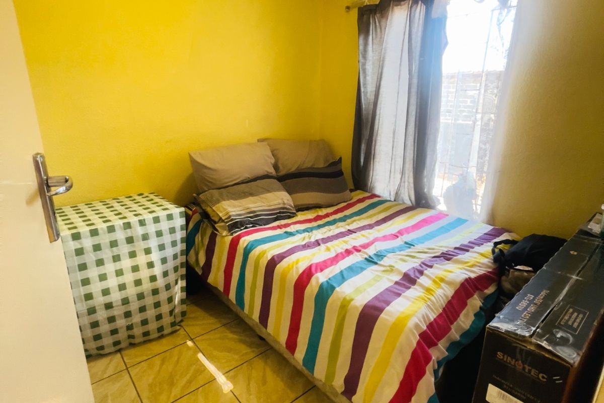 A compact bedroom featuring tiled flooring and a window with security bars, currently finished with bright yellow wall paint.