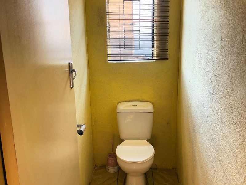 A small, functional bathroom featuring a standard toilet, tiled flooring, and a window with fitted blinds.