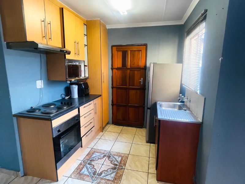 Compact kitchen featuring wooden cabinetry, built-in oven and hob, stainless steel sink, and tiled flooring with a rear access door.