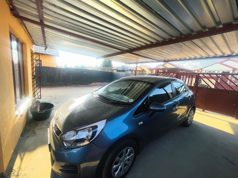 A covered carport area featuring a corrugated metal roof, concrete flooring, and secure perimeter walling with a metal gate.