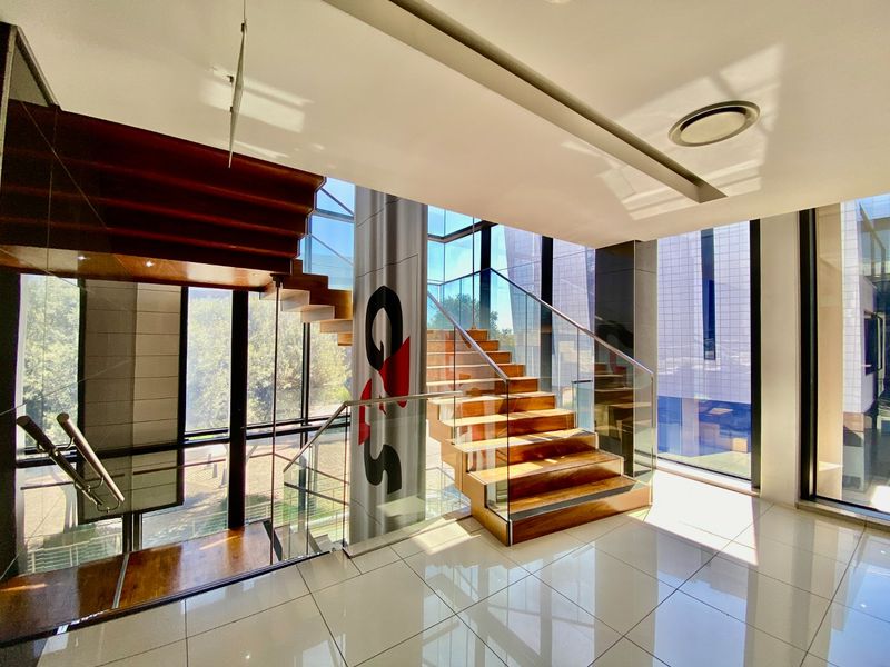 Modern commercial entrance foyer featuring a striking floating timber staircase with glass balustrades, expansive floor-to-ceiling windows, and polished porcelain floor tiles.