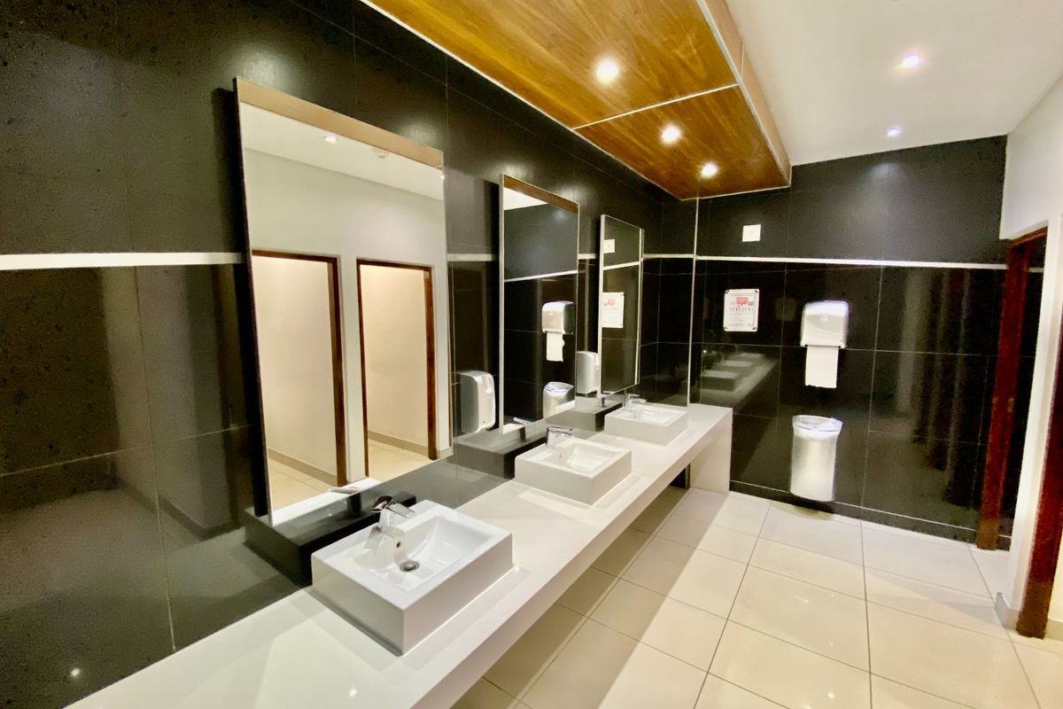 Modern commercial bathroom featuring a triple vanity with vessel sinks, large wall-mounted mirrors, and sleek dark wall tiling with recessed lighting.