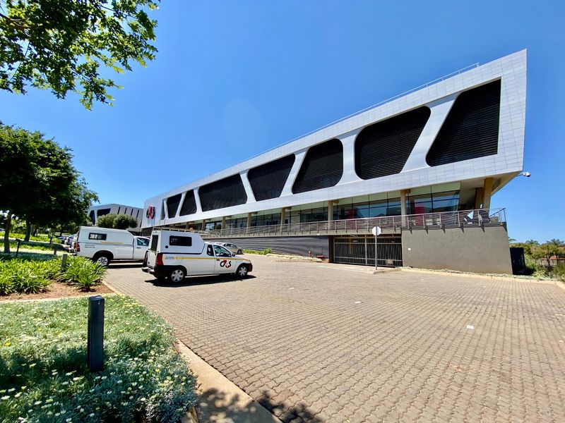 A modern commercial building featuring a distinctive white facade with geometric louvred screens, paved parking area, and secure underground access.