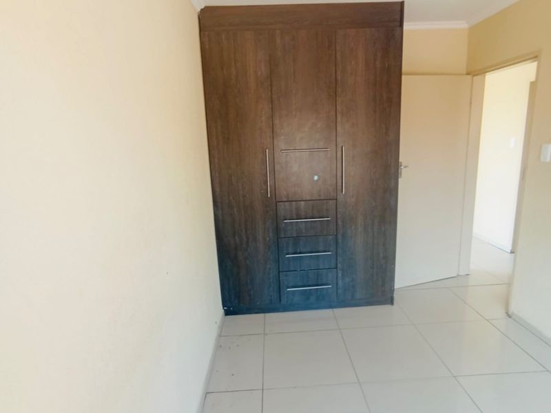 A clean, empty bedroom featuring neutral wall paint, large format floor tiles, and a dark wood-finish built-in wardrobe.