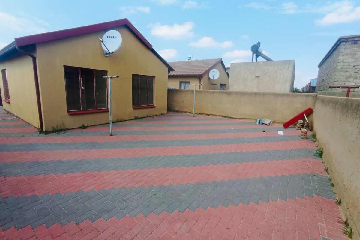 A rear exterior view of the house featuring a paved courtyard, boundary wall, and solar water heating system.