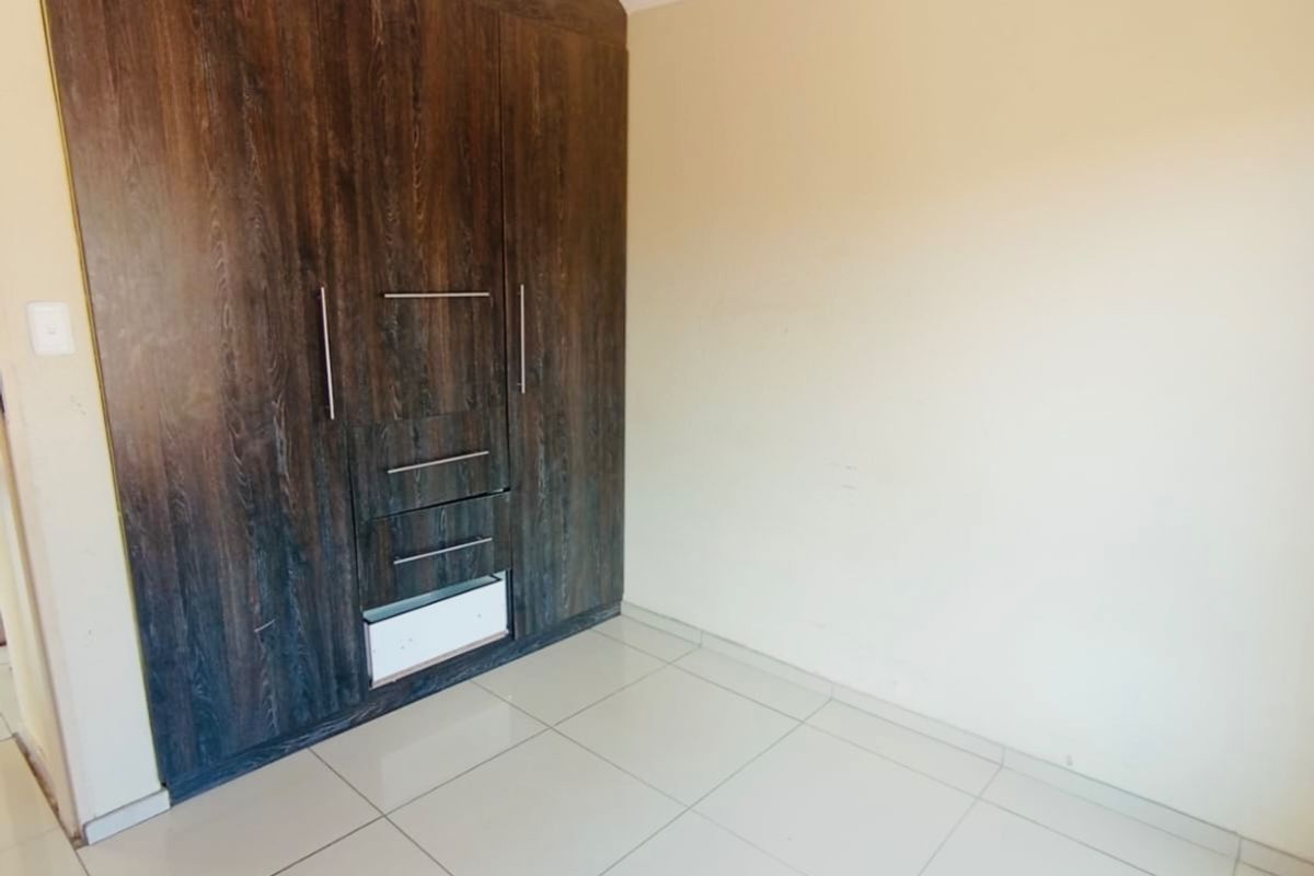 A clean, empty bedroom featuring neutral tiled flooring and dark wood-finish built-in cupboards providing ample storage space.