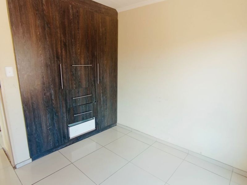 A clean, empty bedroom featuring neutral tiled flooring and dark wood-finish built-in cupboards providing ample storage space.