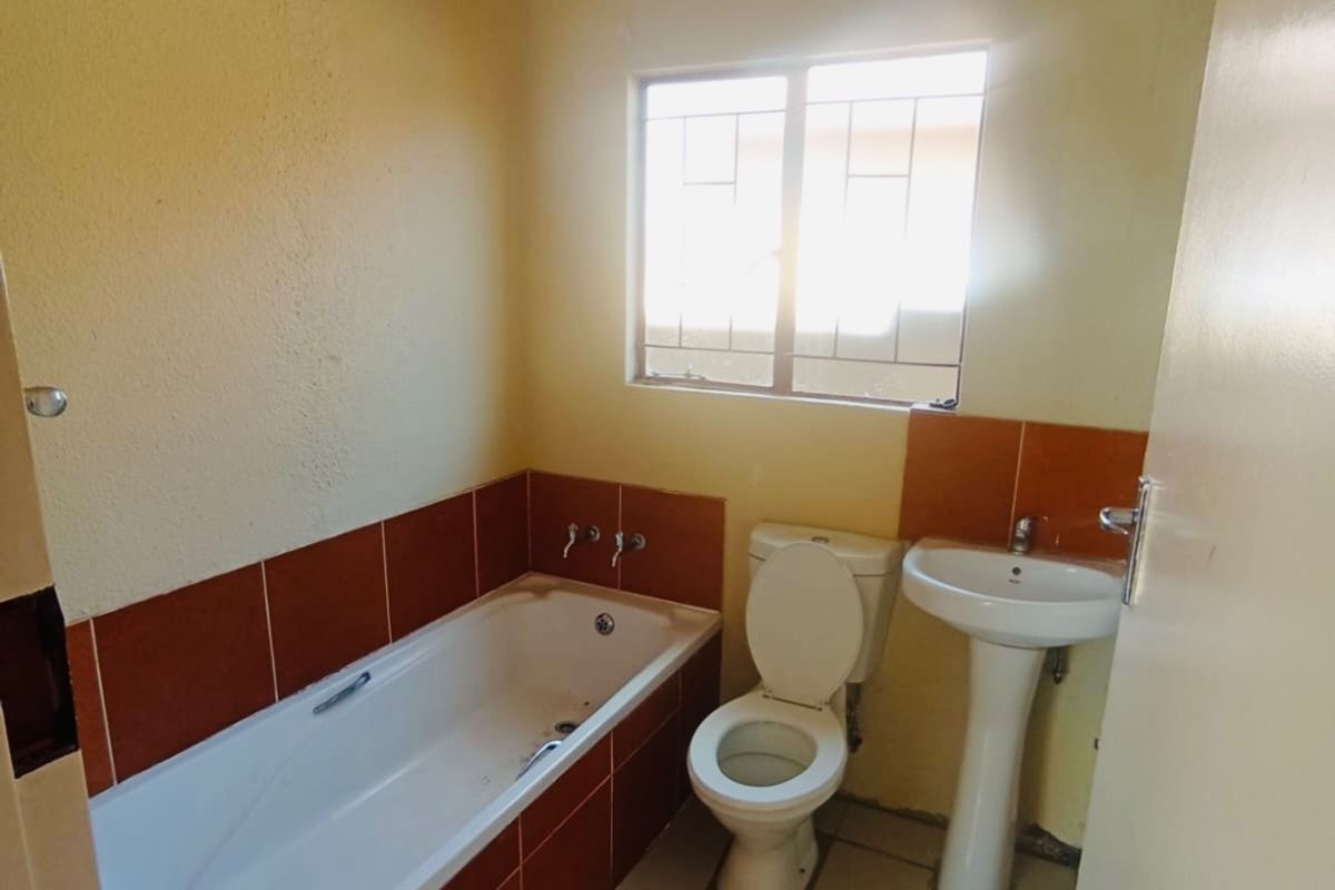 A functional bathroom featuring a bathtub, pedestal basin, and toilet with tiled splashbacks and flooring, offering a blank canvas for modern renovation.