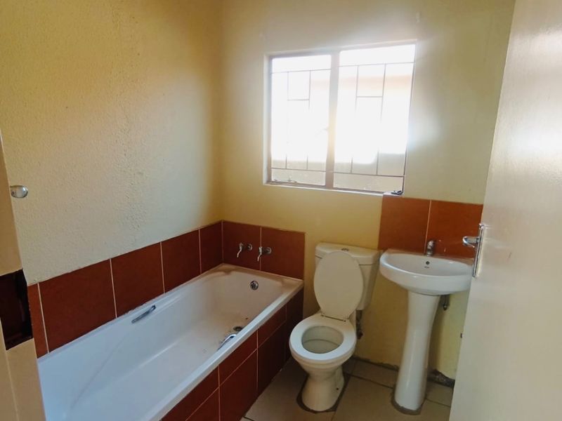 A functional bathroom featuring a bathtub, pedestal basin, and toilet with tiled splashbacks and flooring, offering a blank canvas for modern renovation.