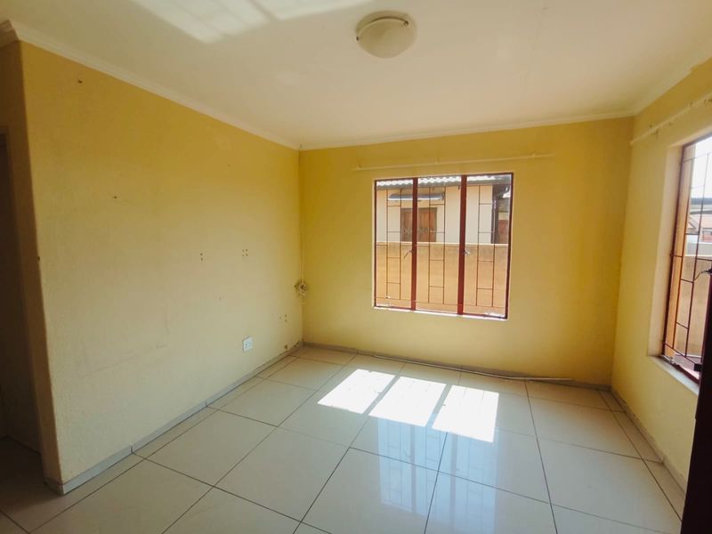 An empty bedroom featuring tiled flooring, yellow painted walls, and windows fitted with security bars.