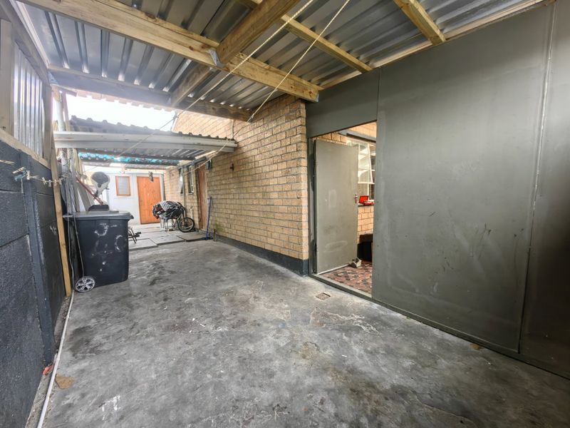 A covered outdoor patio area featuring a corrugated metal roof, timber framing, and face brick walls, providing a functional utility or transition space.