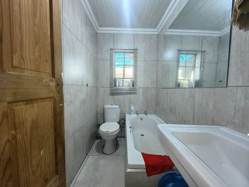 A functional bathroom featuring tiled walls and flooring, a built-in bathtub, a toilet, and a wall-mounted mirror.