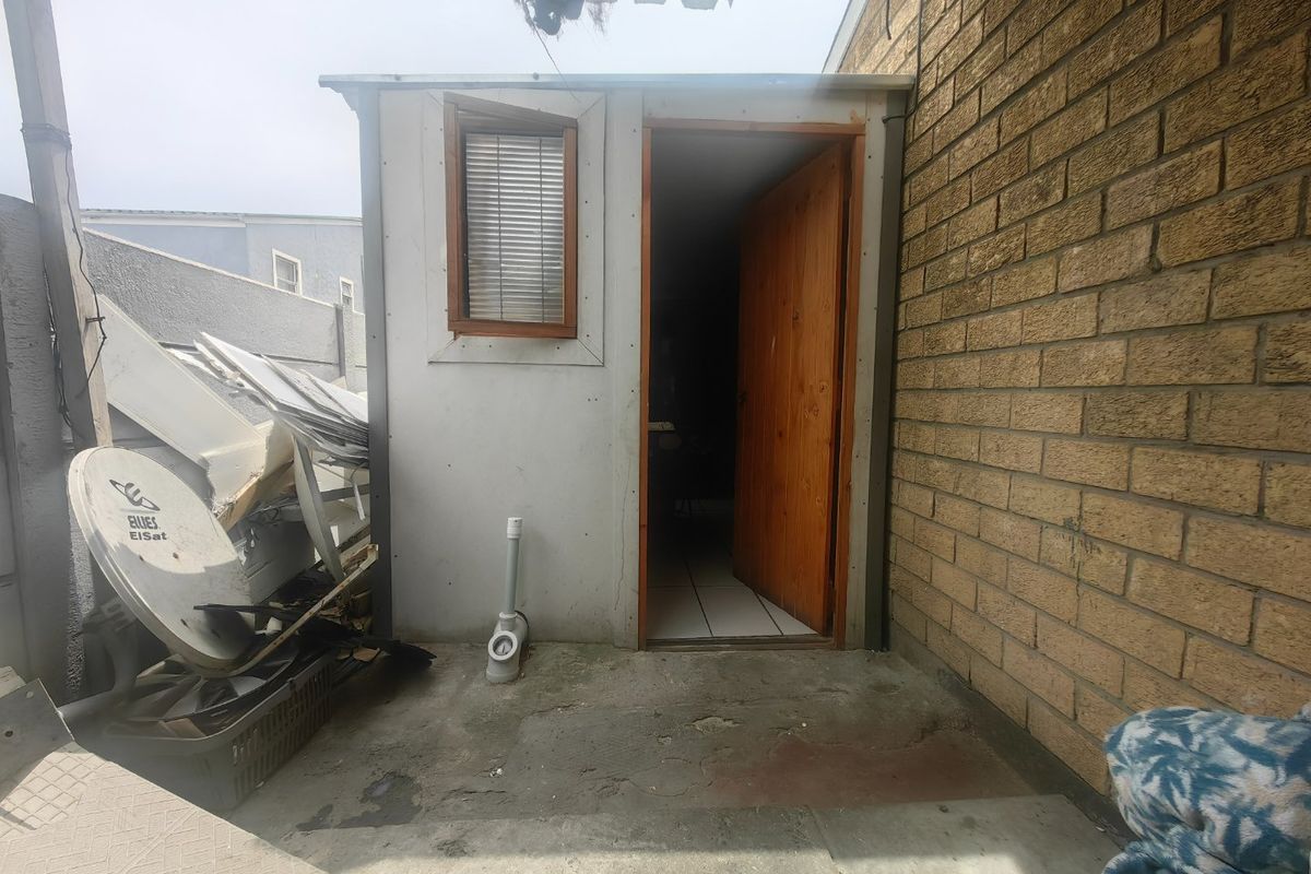 Rear exterior view showing a brick wall, concrete patio area, and a timber door leading into the property.