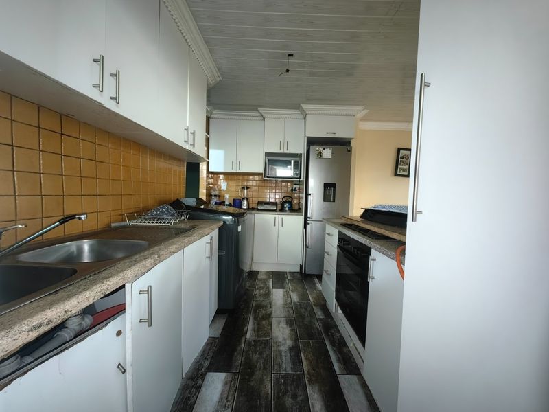 A functional kitchen featuring white cabinetry, tiled backsplash, built-in oven, and wood-look flooring, requiring minor repairs to cabinetry and ceiling fixtures.