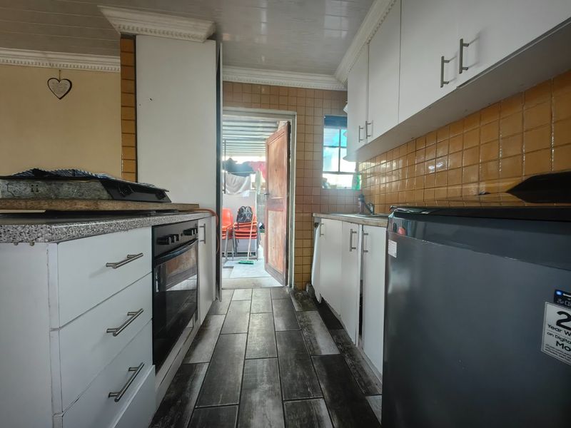 A functional kitchen featuring white cabinetry, built-in oven, tiled backsplash, and wood-look floor tiles, leading directly to an outdoor area.