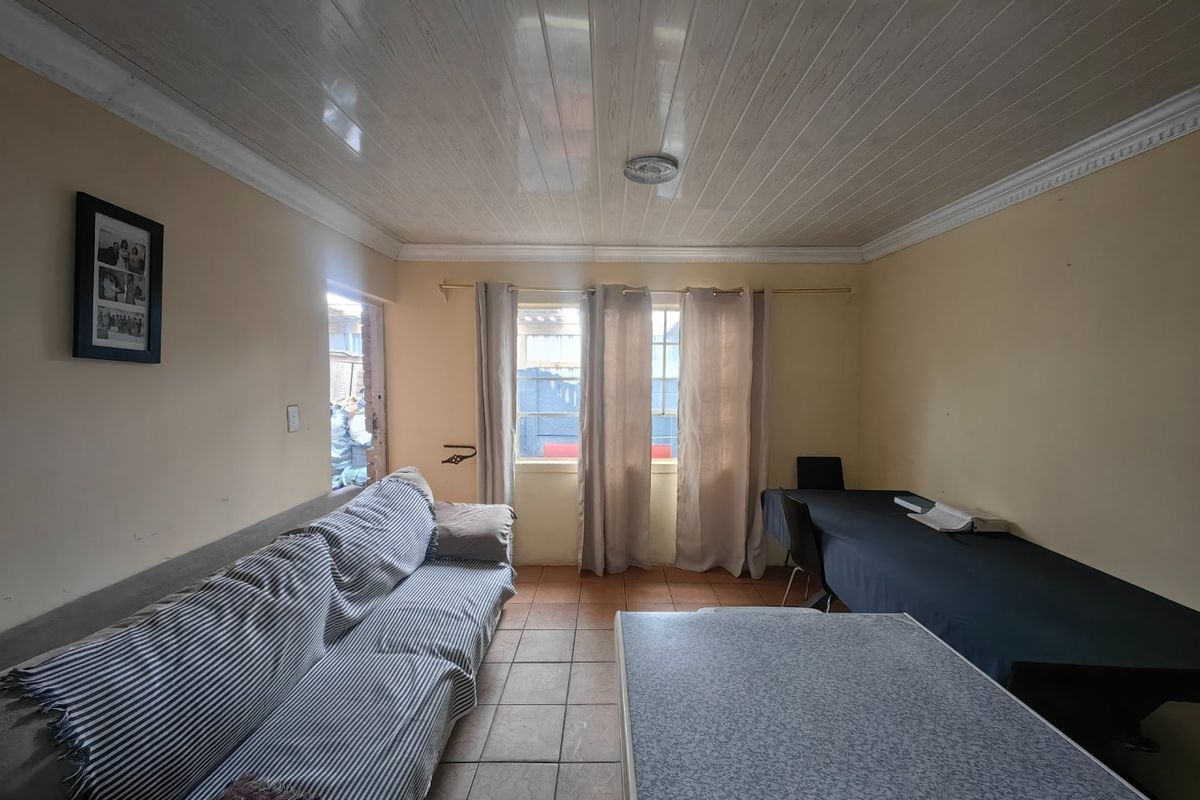 A living room featuring tiled flooring and PVC ceiling panels with decorative cornicing, offering a functional space with potential for modernization.