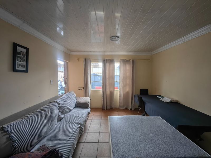 A living room featuring tiled flooring and PVC ceiling panels with decorative cornicing, offering a functional space with potential for modernization.