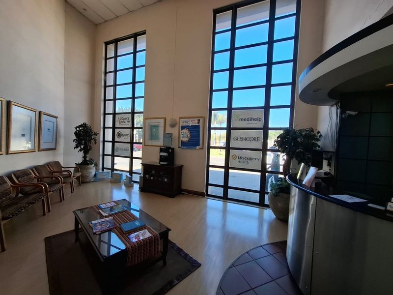A bright and spacious commercial reception area featuring high ceilings, large floor-to-ceiling windows, and a modern reception desk.