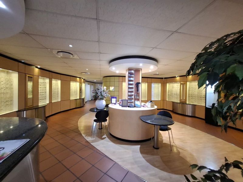 Commercial retail space featuring a central circular service counter, extensive built-in wall display cabinetry, and recessed ceiling lighting throughout the interior.
