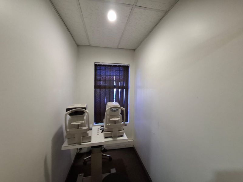 A compact commercial office or examination room featuring a suspended ceiling and window blinds, suitable for professional or clinical use.
