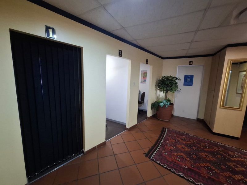 A commercial office hallway featuring tiled flooring, a suspended ceiling, and multiple numbered office entrances.