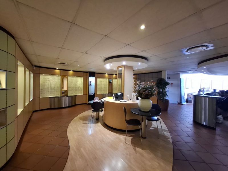 Commercial office space featuring a central service counter, built-in display cabinetry, suspended ceiling with recessed lighting, and a combination of tiled and laminate flooring.