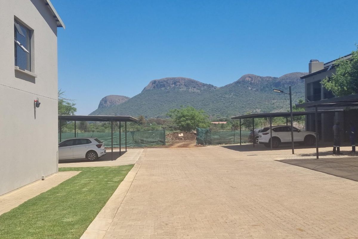 Exterior view of the townhouse complex featuring a paved driveway, covered carport parking bays, and well-maintained lawn areas with mountain views.