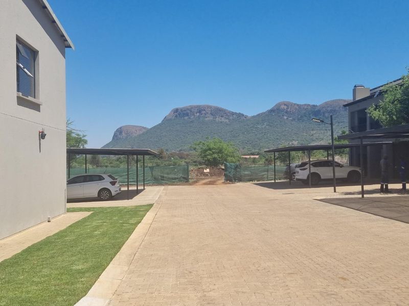 Exterior view of the townhouse complex featuring a paved driveway, covered carport parking bays, and well-maintained lawn areas with mountain views.