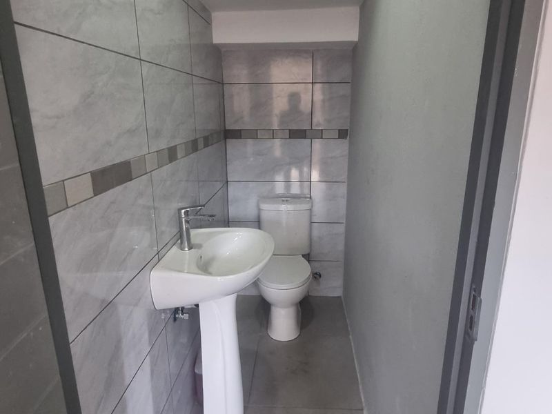 A compact guest bathroom featuring modern grey ceramic wall and floor tiles, a pedestal washbasin, and a standard toilet.