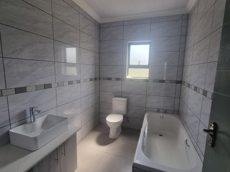 A clean, modern bathroom featuring full-height wall tiling, a vanity with a countertop basin, a toilet, and a built-in bathtub.