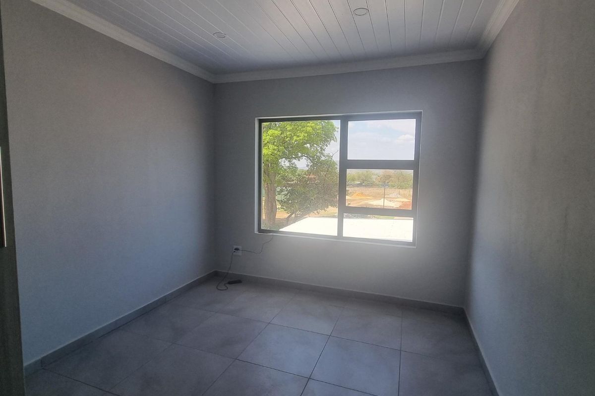 A clean, empty bedroom featuring neutral grey walls, large aluminium window, and modern tiled flooring with a classic tongue and groove ceiling finish.