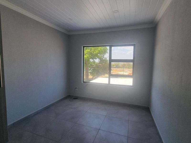 A clean, empty bedroom featuring neutral grey walls, large aluminium window, and modern tiled flooring with a classic tongue and groove ceiling finish.